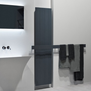 Termoarredo di lusso BIT in alluminio antracite di Antonio Lupi accanto a vasca da bagno moderna con asciugamani decorativi.