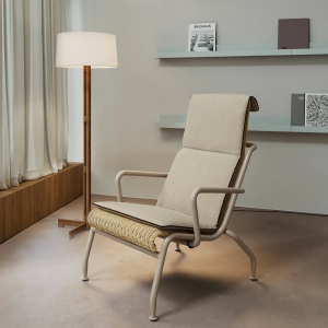 Elegante poltrona lounge Salinas della collezione Eolias di Kettal, con rivestimento in tessuto chiaro, posizionata in un salotto moderno accanto a una lampada da terra e davanti a una mensola con libri di design