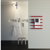 Installazione orizzontale dell'elegante scaldasalviette Rigo in ottone con luce integrata di Antonio Lupi su una parete a righe sottili, con asciugamani in primo piano e una doccia moderna in funzione sullo sfondo.