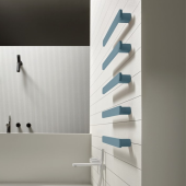 Variante di colore blu del scaldasalviette Rigo in ottone di Antonio Lupi, montato verticalmente su una parete con piastrelle bianche a contrasto, in un ambiente bagno contemporaneo con dettagli neri