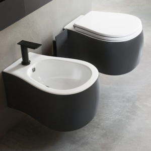 "Sanitari Pear neri e bianchi sospesi di design moderno di Agape su sfondo grigio in cemento, con rubinetto minimalista nero.