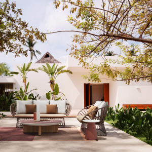 Divano Cala di KETTAL posizionato in un'elegante veranda esterna con vegetazione tropicale e architettura moderna