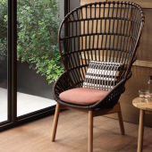 Dettaglio della Poltrona CLUB Cala di KETTAL con cuscino color terracotta, accanto a un tavolino in legno su pavimento in parquet