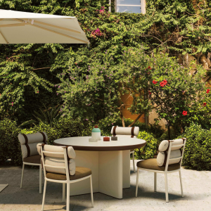 Tavolo Cala di KETTAL in un giardino ombreggiato, con sedie abbinate sotto un ombrellone bianco, immerso in un'ambientazione esterna fiorita."